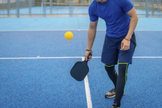 Man strikes a pickleball with his paddle on a vivid blue outdoor court, showcasing athletic