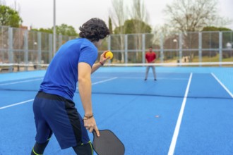 Pickleball player poised to serve on a blue outdoor court facing an opponent, highlighting athletic