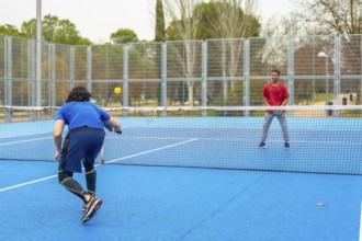 Two men compete in an energetic outdoor pickleball match on a bright blue court, volleying with