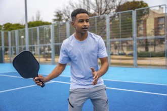 Young man standing on a blue pickleball court, holding a paddle and preparing to hit the ball,