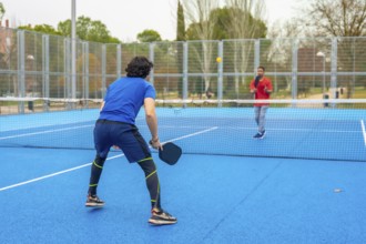 Two male athletes playing an intense pickleball game on a vibrant blue court, holding paddles and