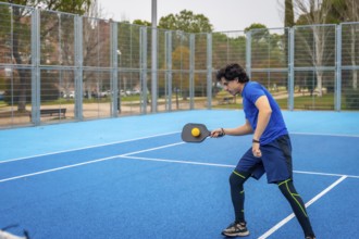 Young man in sportswear hitting a pickleball with a paddle on an outdoor blue court, focused and
