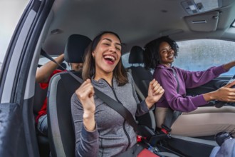 Young diverse friends singing and laughing together in a car on a road trip, sharing joyful