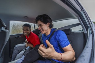 Two smiling diverse men friends wearing sportswear and fasten seatbelt in a car, traveling together