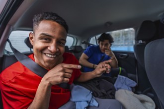 Young friends smiling and pointing from the backseat of a compact car, riding together and