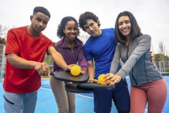 Four happy diverse friends on a bright blue pickleball court, smiling at the camera and holding
