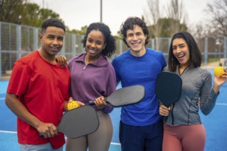 Group of diverse friends standing together on a bright blue pickleball court, smiling and holding