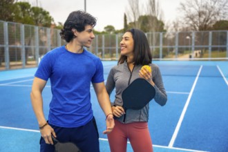 Young man and woman standing together on a vibrant blue pickleball court, holding paddles and ball,
