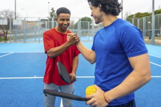 Two male pickleball players shaking hands on a blue outdoor court after a match, showing