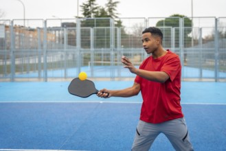 Young man concentrating on returning the ball during a pickleball game on a bright blue outdoor
