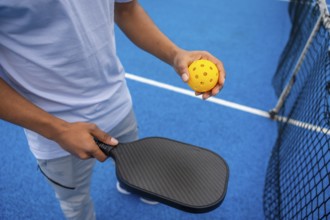 Person standing on a bright blue pickleball court, holding a black paddle and a yellow perforated