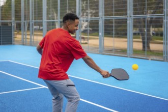 Young athletic man in sportswear striking a pickleball with a paddle on a vibrant blue outdoor