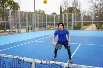 Young man actively playing pickleball on a vibrant blue outdoor court, holding a paddle and