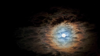 Full moon surrounded by dramatic, colorful clouds in the night sky