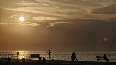 Sunset at sea with silhouettes of people including a fisherman