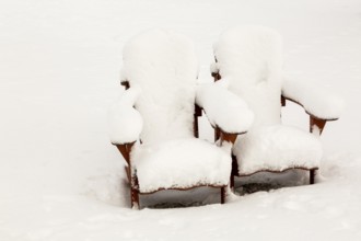 Two brown stained wooden Adirondack chairs covered in freshly fallen winter like snow in public