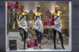Three female, gold-colored mannequins in a women's clothing store, posters, clearance sale due to