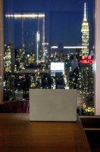 Laptop resting on a wooden desk, overlooking the illuminated cityscape of manhattan and the iconic