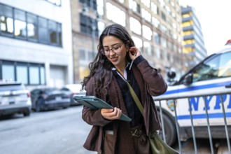 Young businesswoman in glasses walking manhattan streets, focused on her digital tablet while