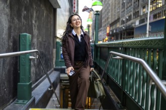 Young businesswoman smiling while emerging from a subway entrance in manhattan, carrying a