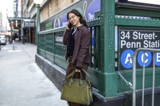 Young businesswoman in a brown jacket and glasses stands on a manhattan sidewalk near penn station,