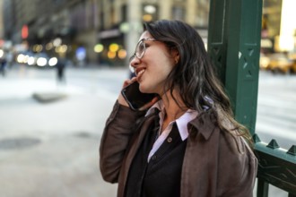 Young businesswoman smiling while talking on a smartphone, having a pleasant conversation standing