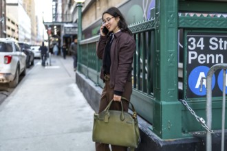 Young businesswoman walking on a new york city street, talking on her smartphone, carrying a