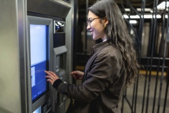 Young businesswoman standing at a subway station, operating an automated ticket machine to purchase