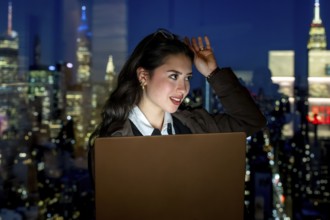 Young businesswoman working on laptop, thinking and looking away from a high rise office window at