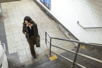 Young businesswoman walking down subway station stairs, checking her smartphone while holding a