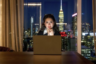 Young businesswoman with glasses on her head, focused on her laptop in a high rise at night,