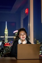 Young asian businesswoman focusing on her laptop screen, working late from an office with the