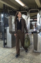 Young professional woman in glasses and olive bag passing a manhattan subway turnstile, navigating