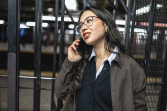 Young businesswoman in glasses talks on smartphone while waiting for a manhattan subway,