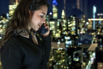 Young businesswoman smiling while talking on a mobile phone with a blurred illuminated new york