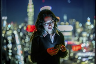 Young businesswoman smiling, reading a message on her glowing smartphone, standing by a window with