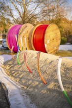 Colourful cables stick out of a snow hill, behind them colorful rolls of cable in winter light,