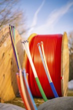 Colourful cables in a wintry environment in front of large, red cable spools, fibre-optic