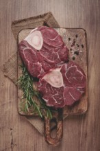 Knuckle on the bone, raw meat for ossobuco, on a wooden chopping board, with a sprig of rosemary,