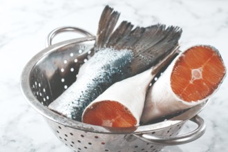 Fish tails are placed in a colander on a marble counter. The colander allows water to drain away