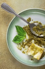 On a platter is a pesto sauce made from fresh basil, with a slice of bread and a spoon on a plate.