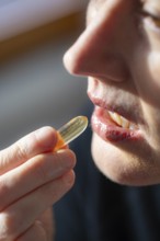 Face of a woman taking one omega capsule. Germany