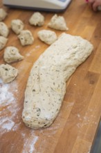 A large lump of dough and small pieces of dough on a floured wooden table, baking rolls,