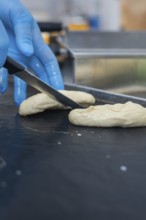 A person in gloves cuts dough with a knife in the bakery, baking rolls, Haselstaller Hof,
