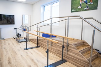 A bright room with rehabilitation equipment, including stairs with handrails, an ergometer game and