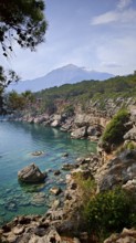 Rocky coast with clear blue water and view of snow-capped mountains in the background, view of