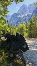 A bicycle on a dirt road in an alpine landscape with mountains and forests in the background,