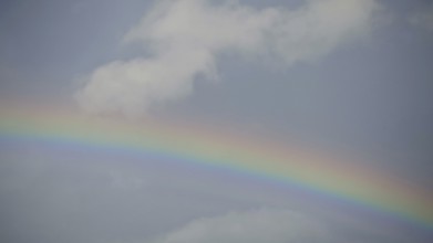 A vivid rainbow against a blue sky with light clouds, Rennsteig, Germany