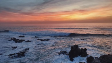 Dramatic sunset over the sea with waves crashing against black rocks, Southwest Alentejo Natural