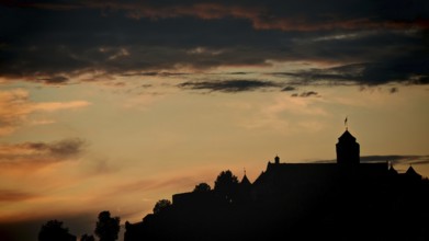 A castle silhouette against a dramatic, cloudy sky at sunset, Rosenberg Fortress, Kronach, Germany
